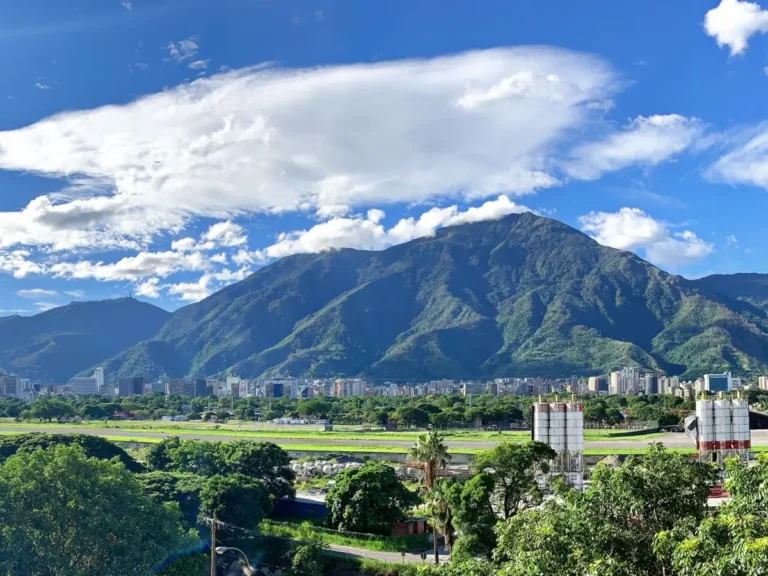 Cerro El Ávila bajo un cielo azul con nubes, con edificios y vegetación de Caracas al pie de la montaña