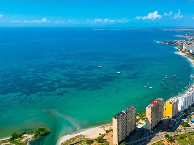 Vista aérea de la costa de Porlamar con mar turquesa, arena clara y edificios frente a la playa